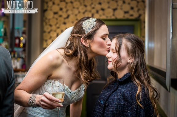 A bride kissing the head of her flower girl after luxury makeup application