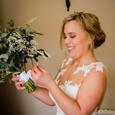 A Wrexham Bride smiling with her bouquet on her wedding day showing her natural makeup side profile.