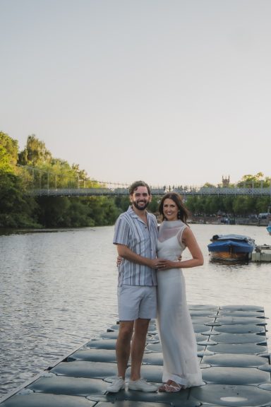 On the River Dee in Chester, bride and groom smile at the camera, showing off their summer bridal party