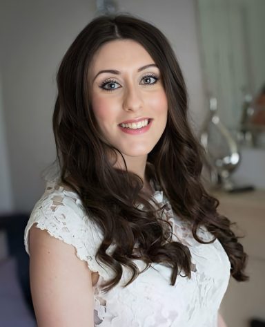 Bride smiling at the camera in her Wrexham home before travelling to her wedding in Cheshire, after her professional bridal makeup. 