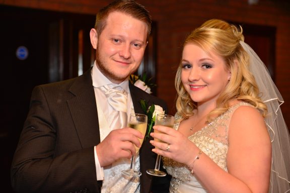 A happy couple pose with Champagne at their Mold wedding ceremony. The bride has beautiful, bridal makeup and glowing skin. 